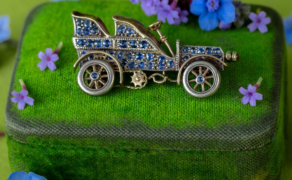 A vintage sapphire automobile brooch styled on a velvet jewelry box, the kind of estate piece where fine jewelry brooch demand has concentrated for six years