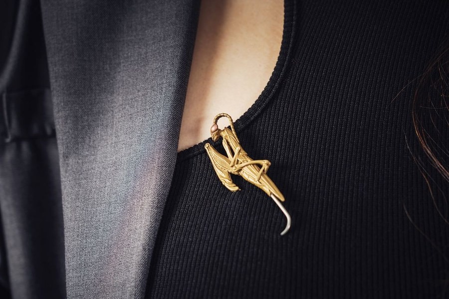 A single sculptural gold brooch worn high on the lapel near the shoulder, showing brooch placement near the lapel notch