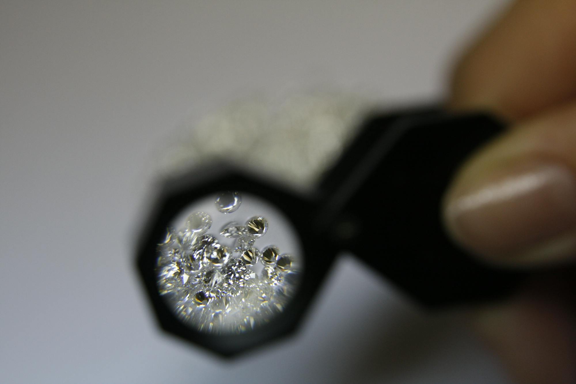 A jeweler's loupe held over a parcel of small loose diamonds, illustrating the kind of stone-by-stone sorting gemological labs perform when undisclosed lab-grown material turns up in natural-diamond parcels