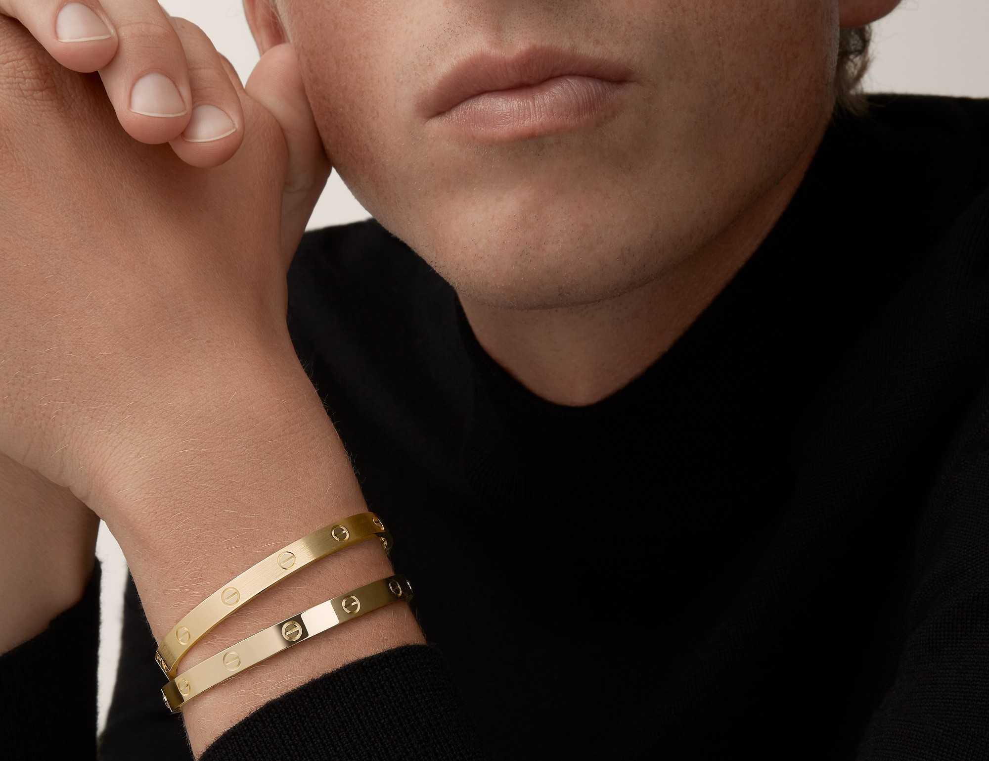 Two Cartier Love bracelets in yellow gold stacked on a wrist, worn with a black turtleneck. Image courtesy of Cartier.