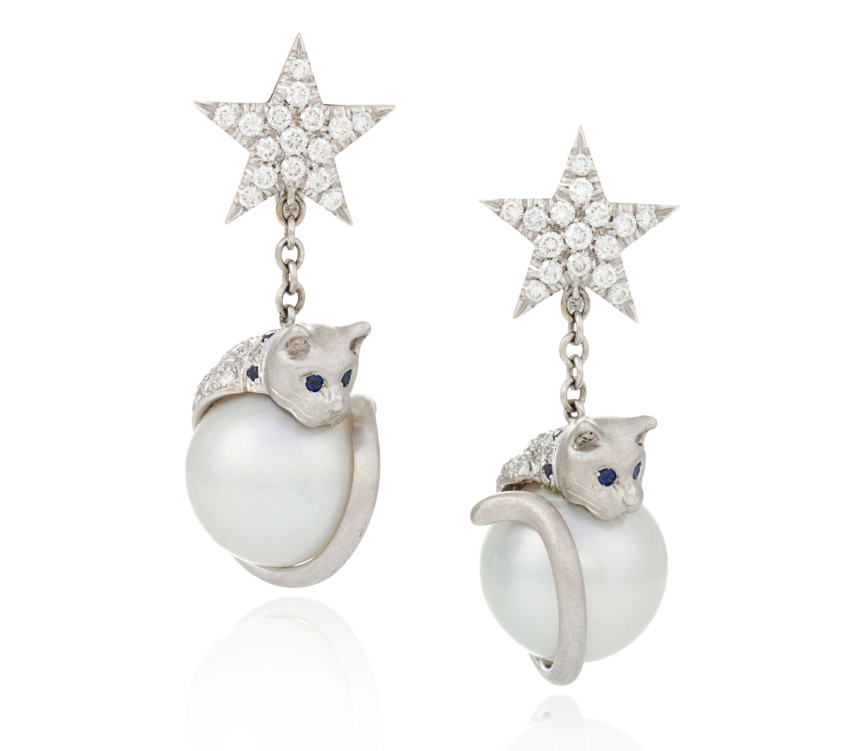 A pair of 18K white gold cat earrings, each cat curled around a 15mm South Sea pearl with sapphire eyes, under a diamond star top — lot 59, the cats you can actually wear