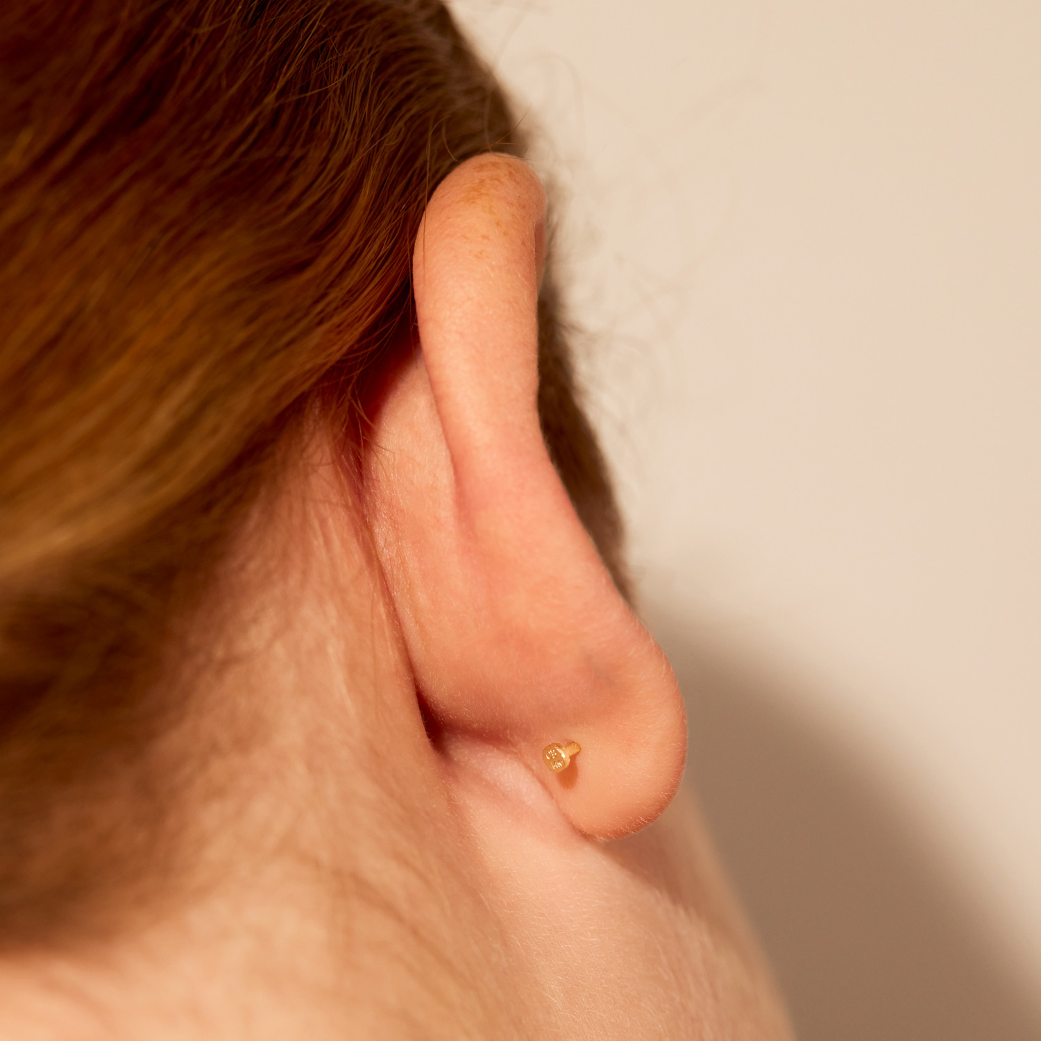 A single 14k gold flat-back diamond stud worn in a lobe, seen from the side, the kind of often-neglected placement that reads as considered.