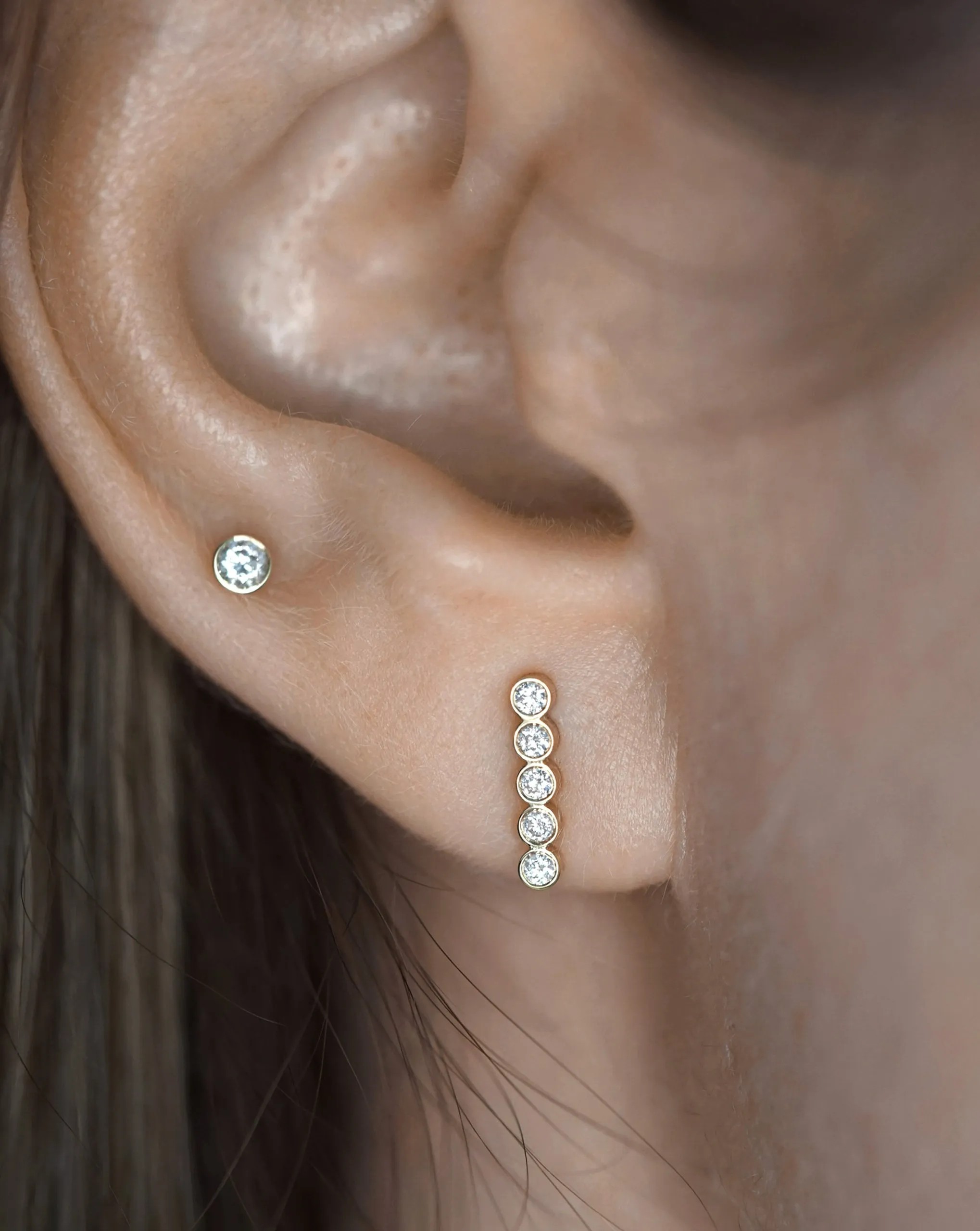 A bezel-set diamond bar climbing the lobe in solid gold, close enough to read the settings, the construction quality fine jewelry buys in the upper ear.
