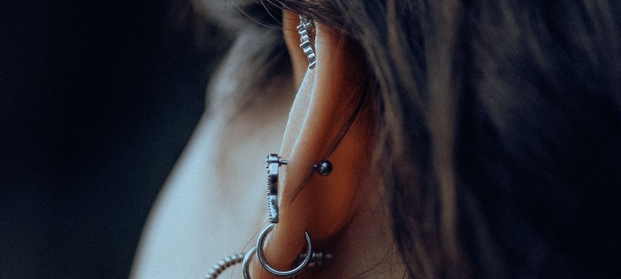 A close side profile of an ear wearing a composed lobe stack of silver hoops and cartilage studs, a curated ear in fine jewelry.