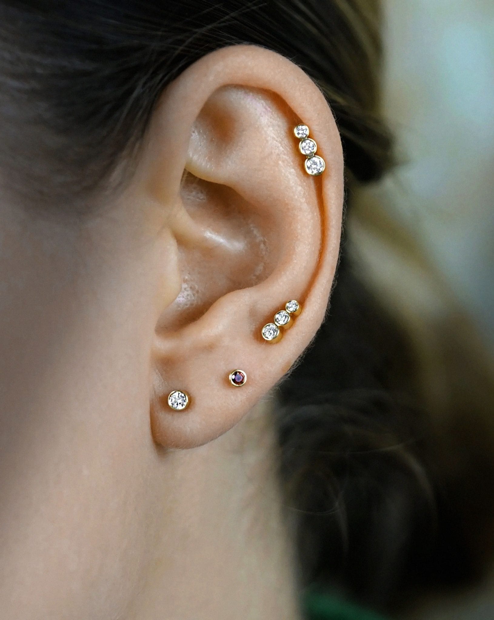 A curated ear of gold bezel-set diamond studs climbing the helix and upper lobe above a single lobe stud, three zones with one clear focal point.