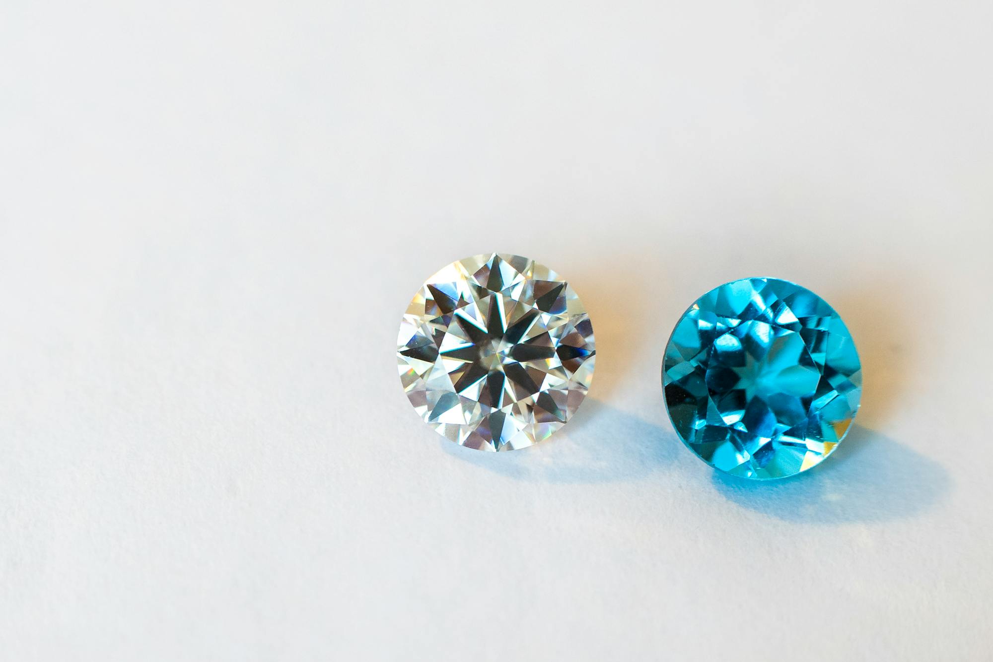 Two loose round-brilliant stones on a white surface, one colorless and one blue