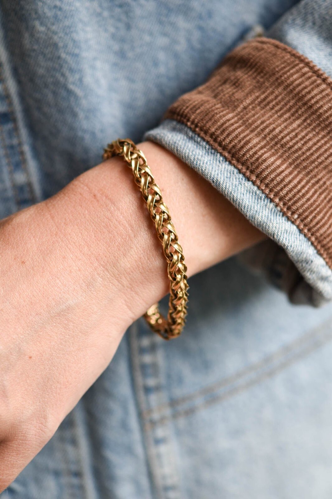 A heavy Victorian woven-link 14k gold bracelet worn on a wrist over a denim jacket, the kind of solid-gold weight and labor-intensive construction the price doesn't reflect, courtesy of Erstwhile Jewelry