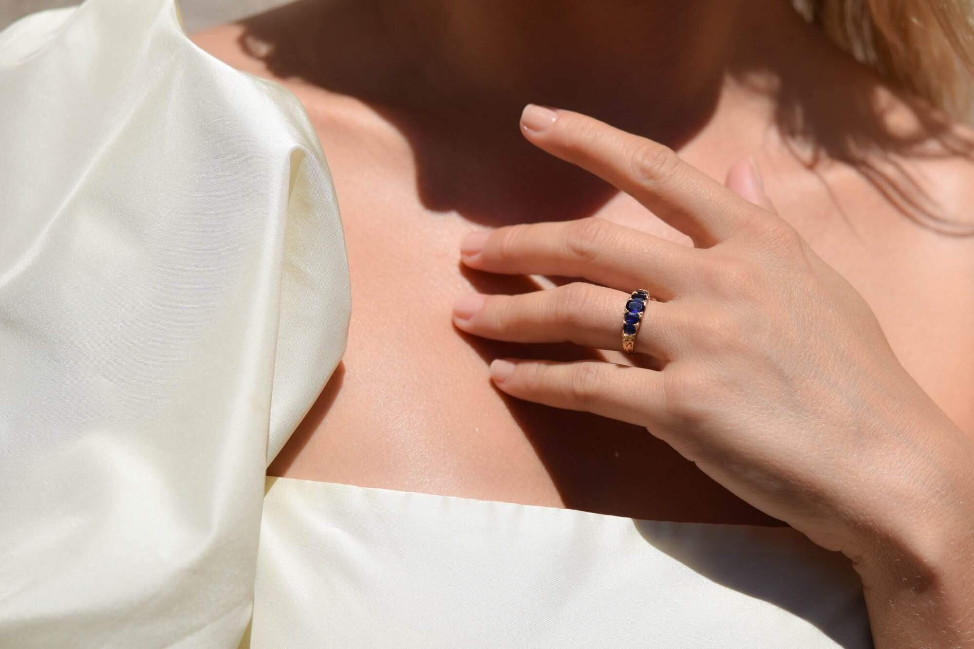 A 19th-century Victorian five-stone sapphire ring in 18k gold worn on a hand resting at the collarbone, the kind of unsigned estate piece that gives you more ring for less money, courtesy of Erstwhile Jewelry