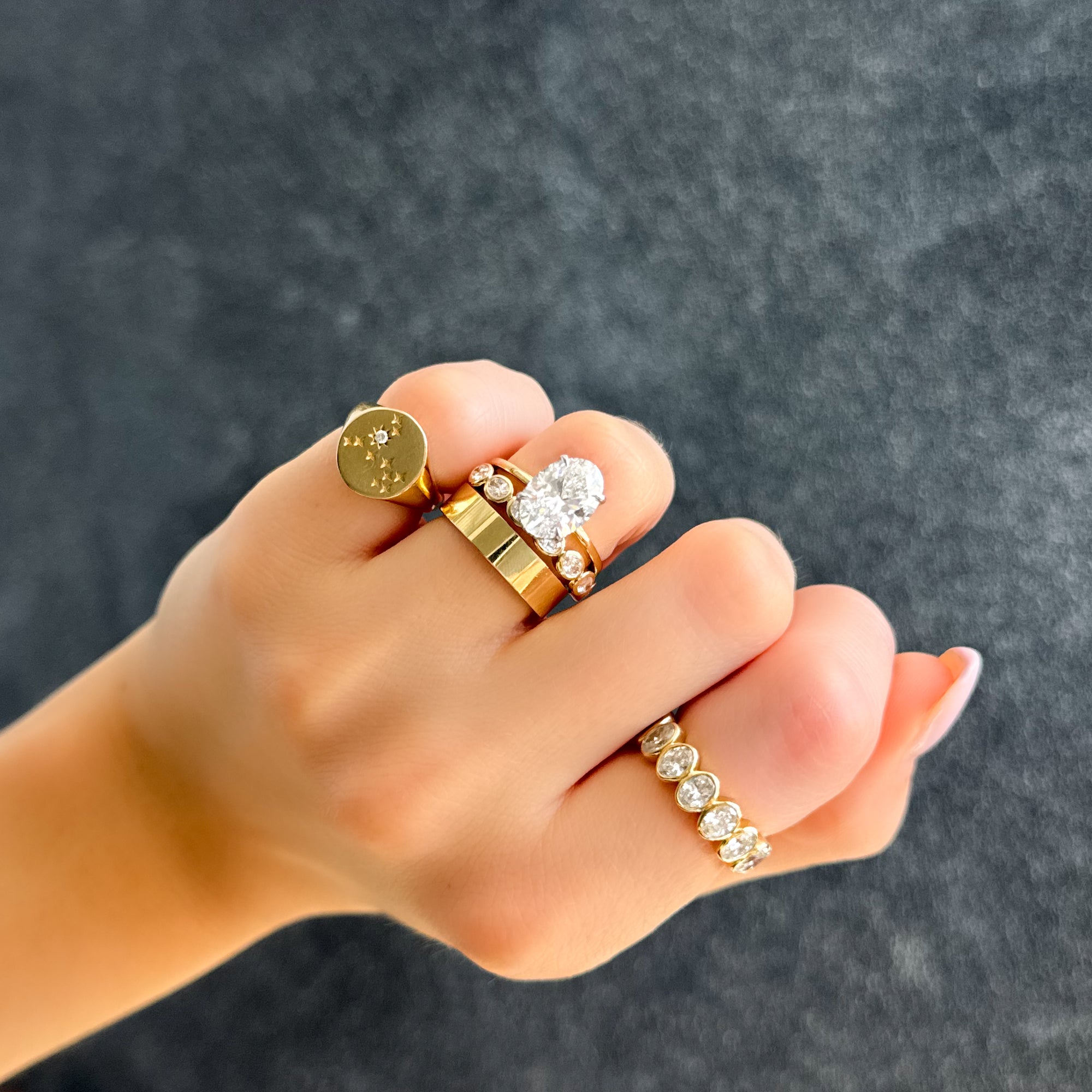 A stack of GOODSTONE rings worn on a hand (a gold signet, an oval-diamond solitaire, and a bezel-set diamond band), from a maker that builds each ring around the customer with full documentation