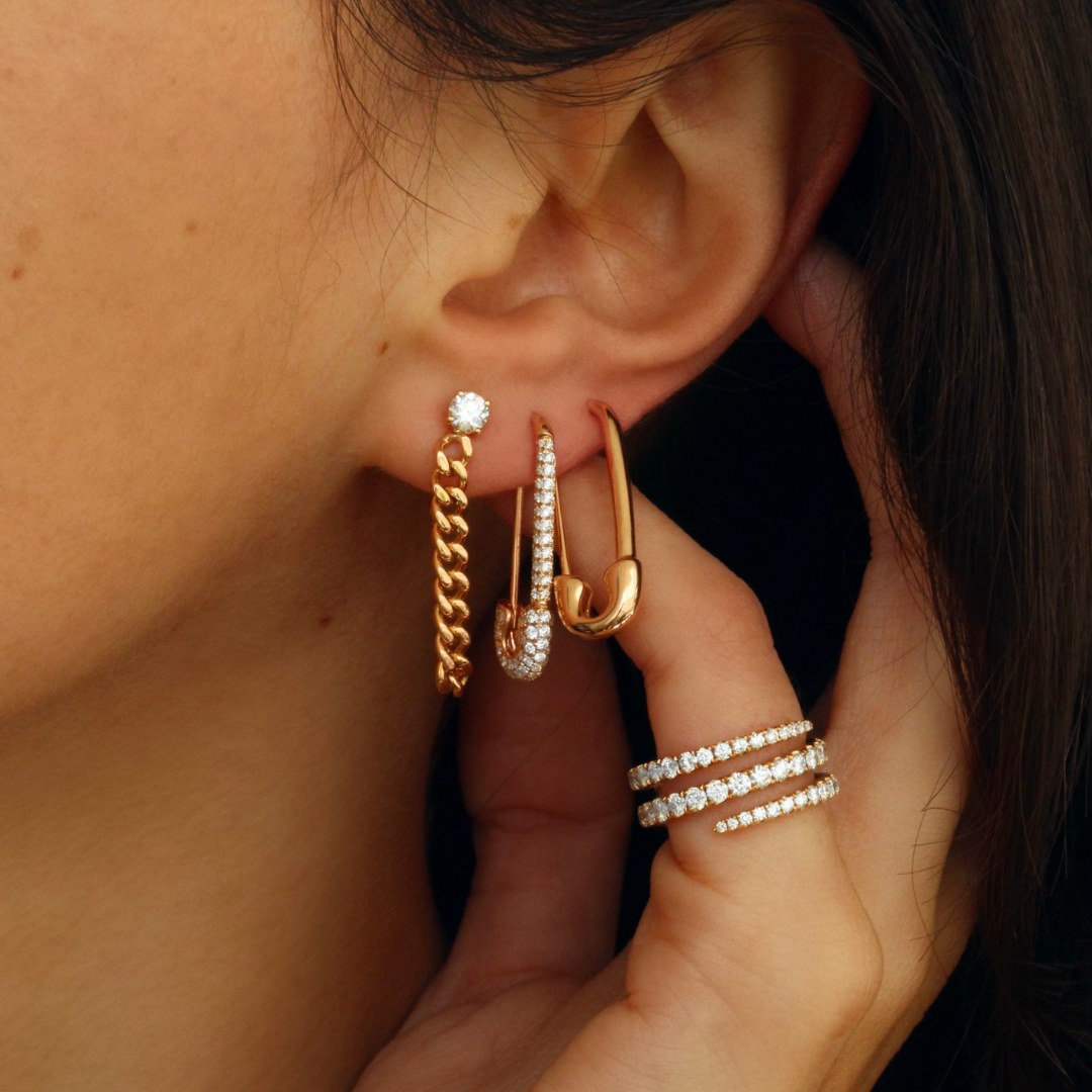 Anita Ko's plain gold safety-pin earring worn in the ear beside a pave huggie, the safety-pin vocabulary sold by the single that the resale market chases while the deep-diamond one-offs discount hard.