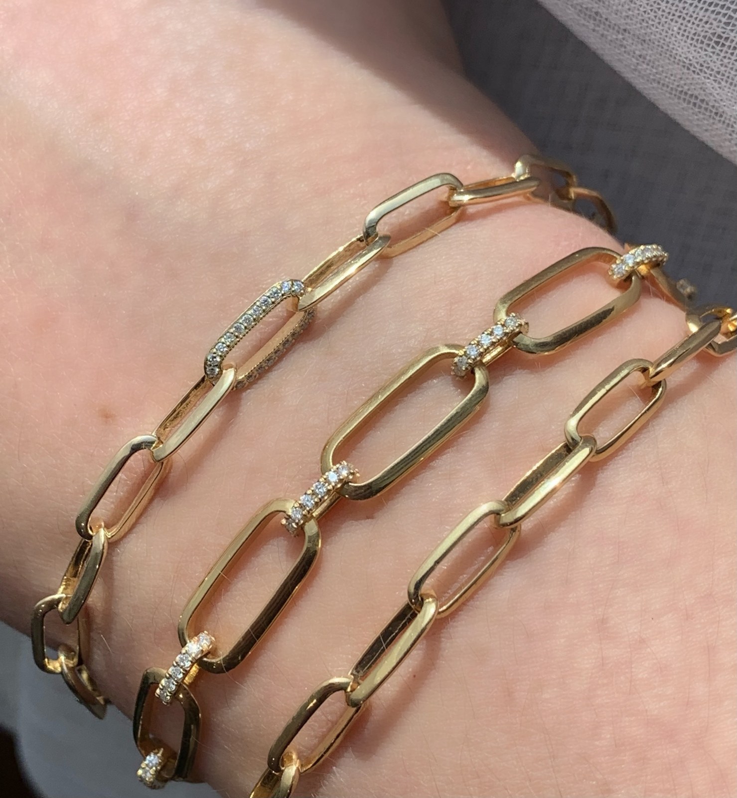 Lizzie Mandler's knife-edge oval link chains stacked on a wrist, one pave link among plain gold, the sharp triangular ridge catching the light down each link, the signature silhouette whose bracelet is the in-tier buy the resale market rewards.