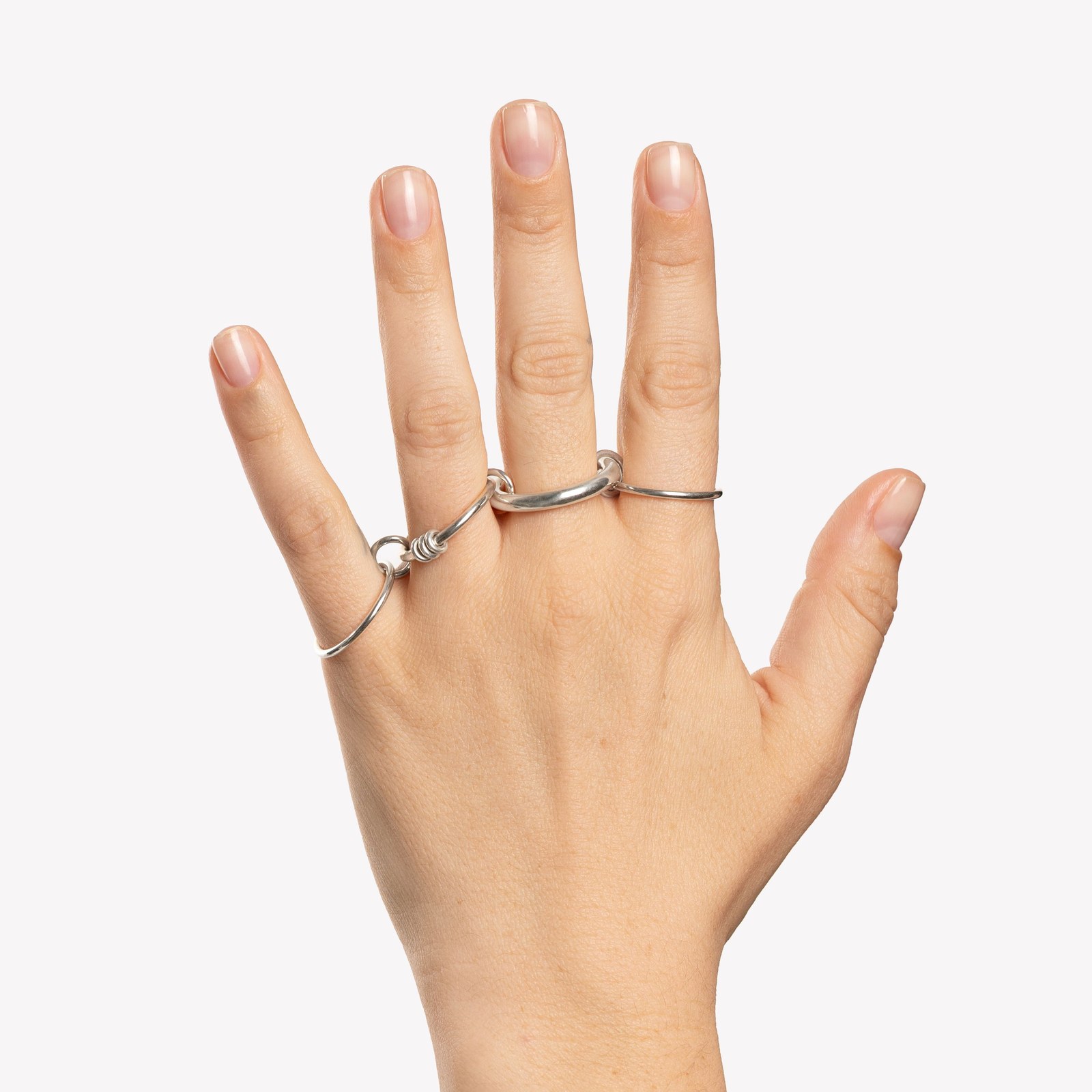 Two plain silver Spinelli Kilcollin linked rolling rings worn spread across the fingers, the recognizable orbiting-band silhouette in the affordable core version the used market keeps paying near retail to own.