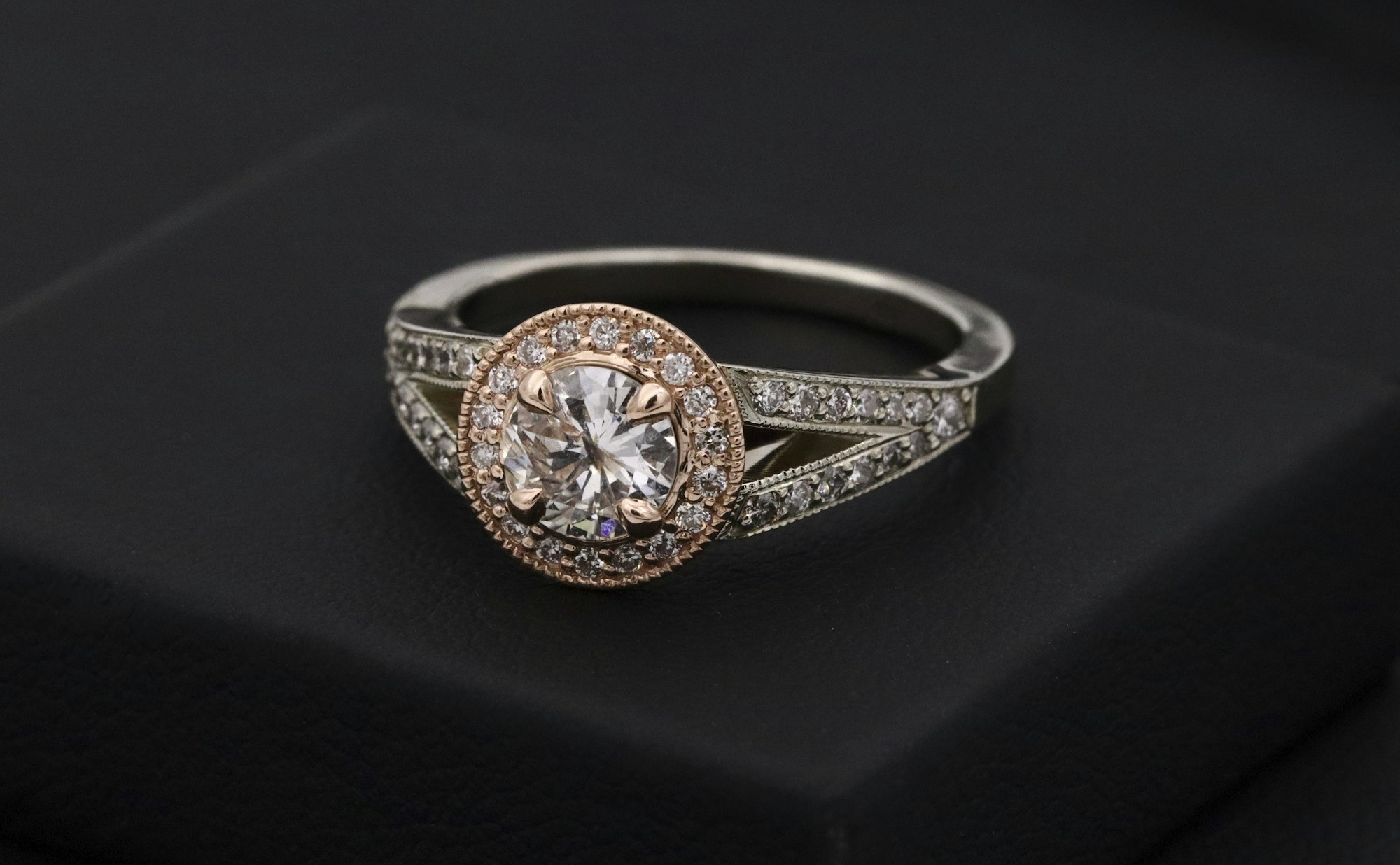 A lab-grown diamond solitaire engagement ring with a rose-gold halo, photographed on a dark surface