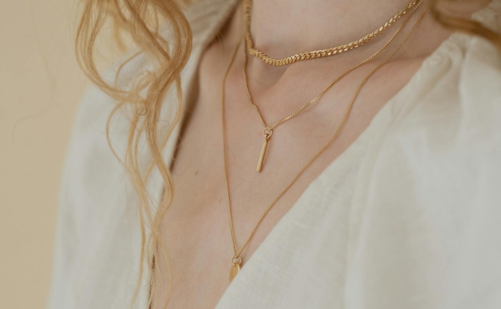 A layered stack of fine gold necklaces worn at the neck, a few cohesive pieces spaced so each one reads clearly, the kind of stack someone who knows jewelry can read across a room.