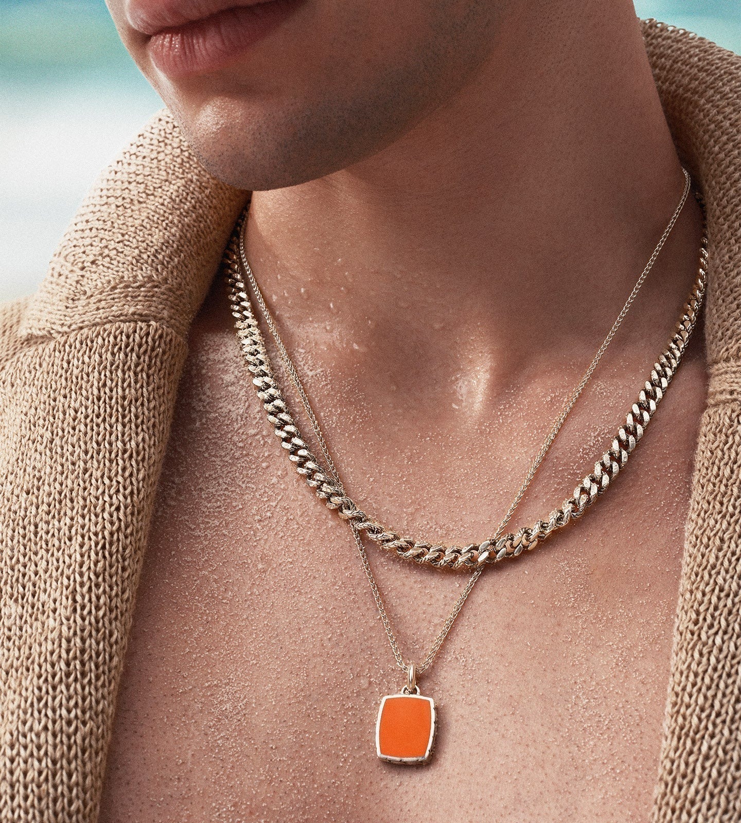 A man wears a solid gold curb chain layered with a fine gold pendant chain over an open knit, the gold chain bought as a chain in its own right and worn as a daily signature