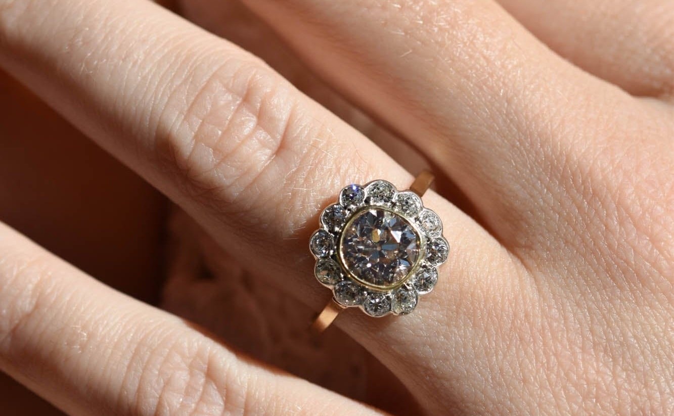 An antique Victorian old mine cut diamond cluster ring worn on a hand, its warm center stone glowing against a white-diamond halo