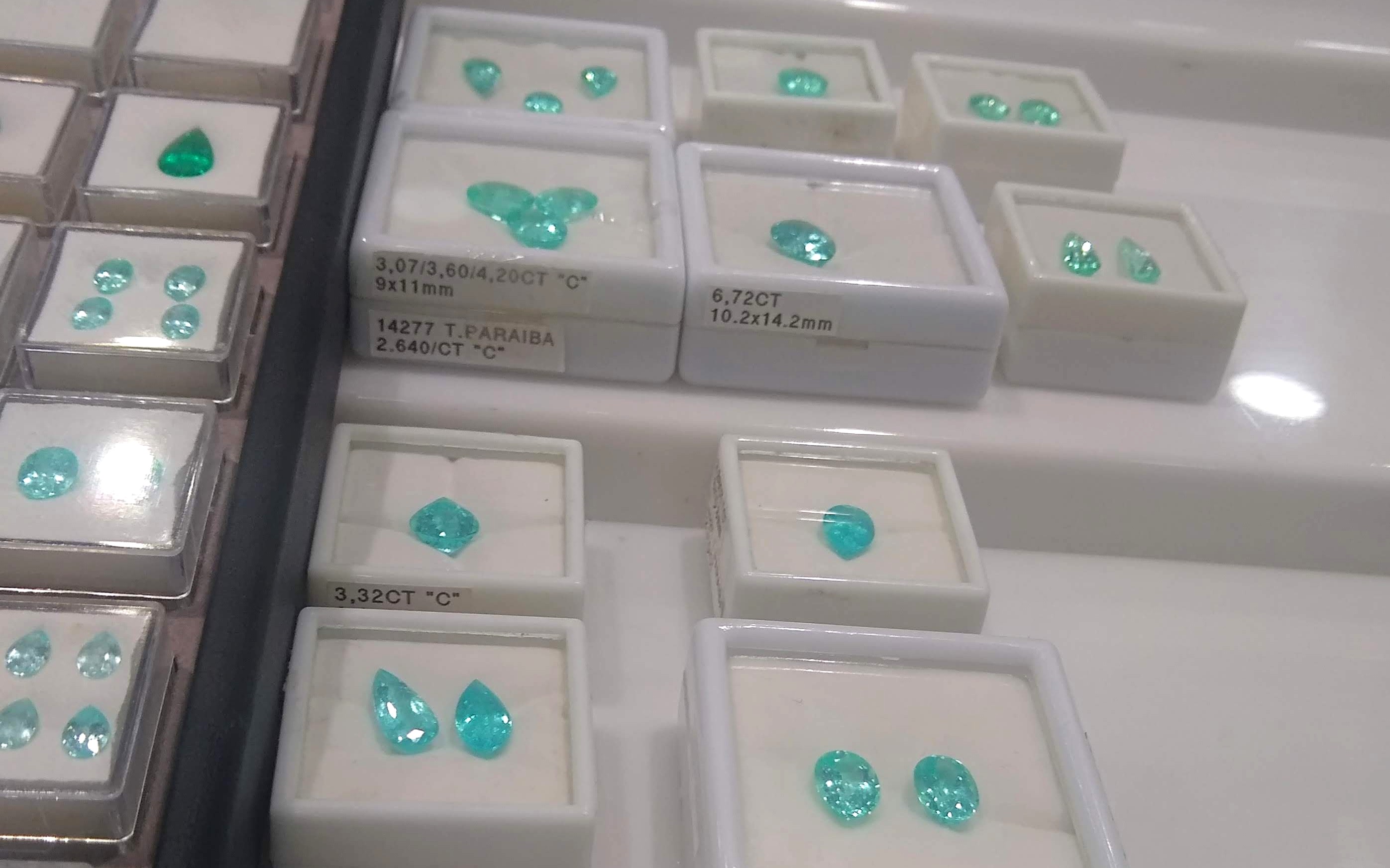 Loose neon blue-green Paraíba tourmalines in dealer parcel boxes with carat labels, the loose-stone market an accessible budget shops.