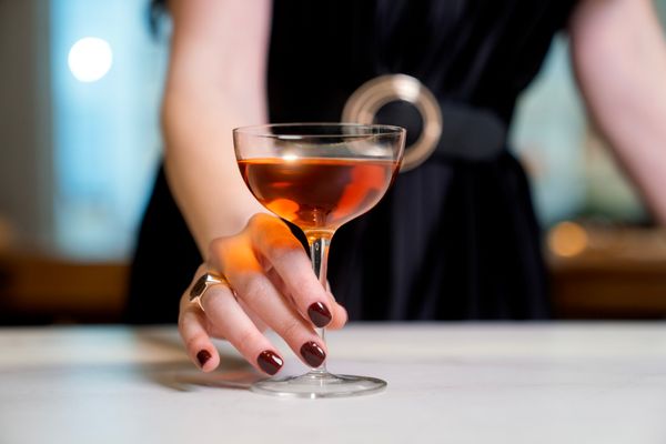 A ringed hand holding a cocktail at a marble bar, jewelry chosen and paid for by the wearer