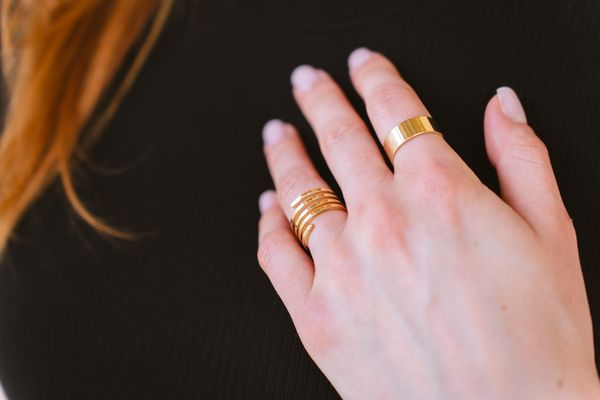 A woman's hand wearing a stack of gold rings, jewelry accumulated and owned by the wearer herself