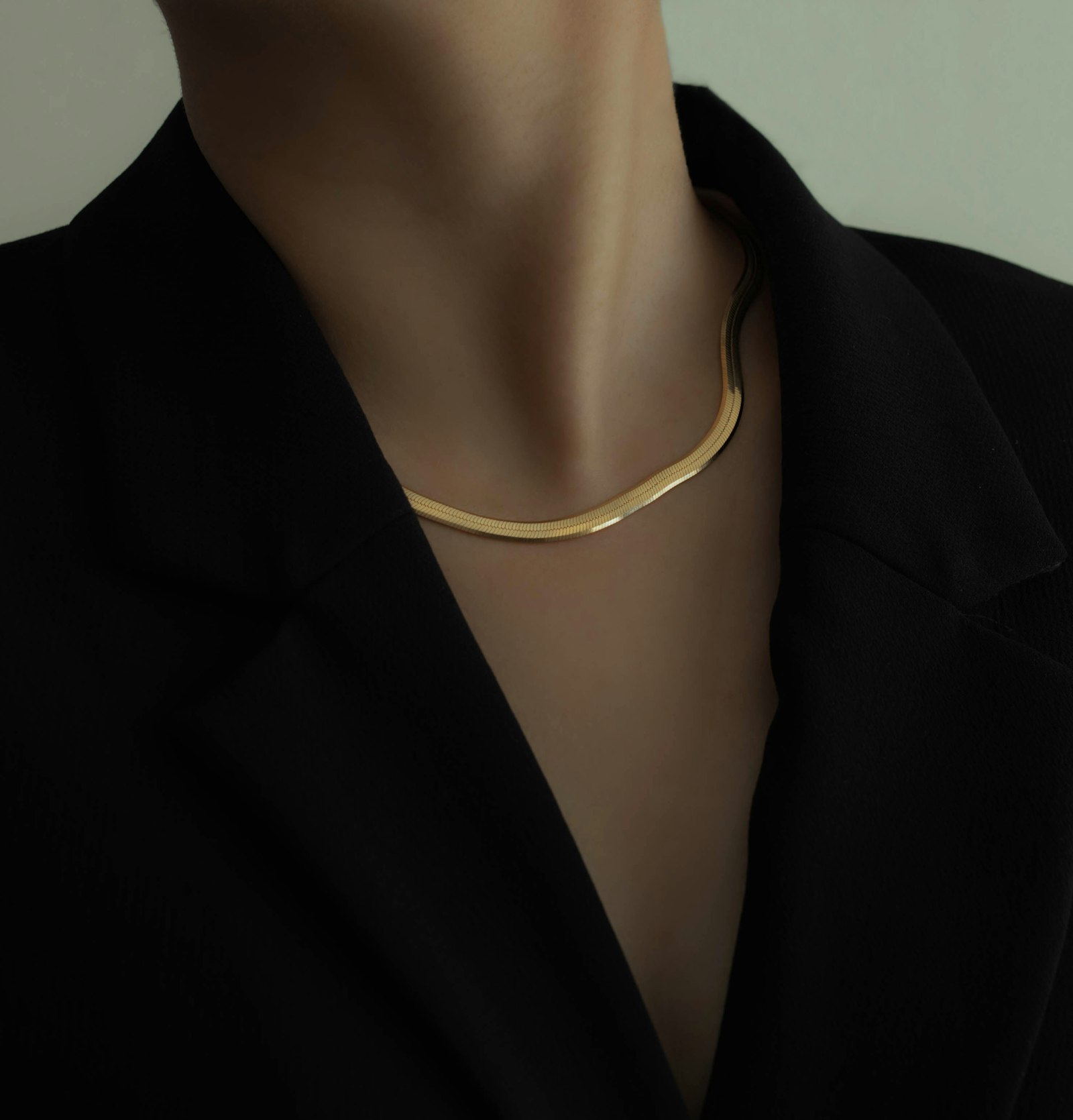 A gold herringbone chain worn on a bare collarbone under a black blazer, photographed as the buyer's own choice rather than a brand campaign