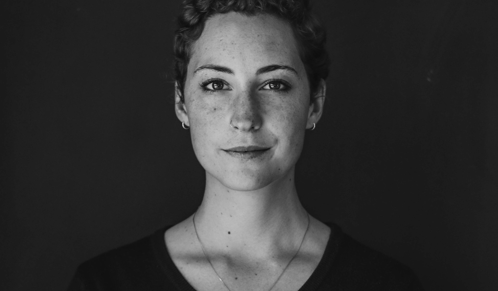 A direct black-and-white portrait of a woman wearing a fine necklace and looking straight at the camera, no longer the recipient in the ad but the buyer who shops for herself