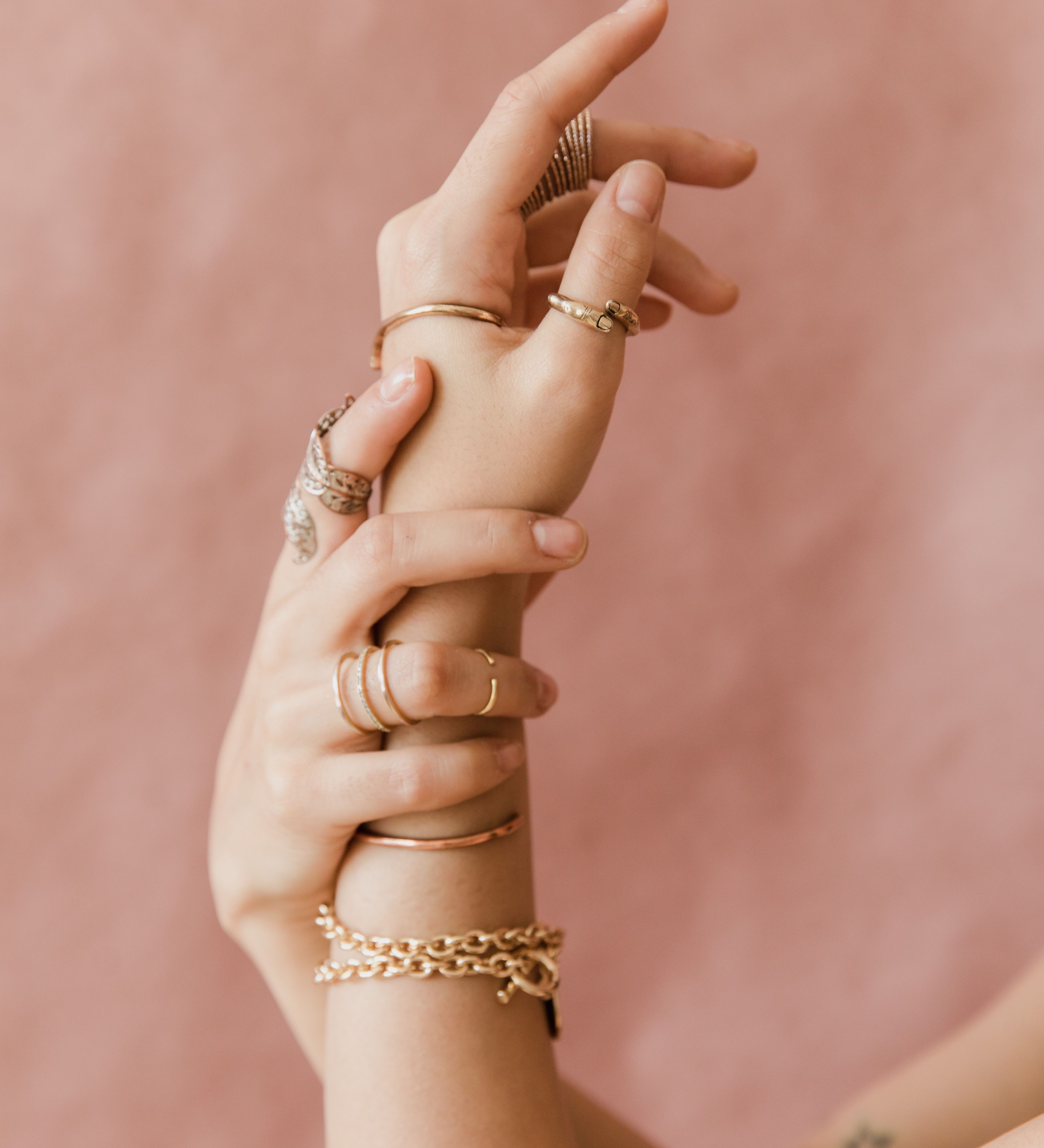 Two hands layered with thin solid-gold bands and a gold chain bracelet, the everyday fine-jewelry bar of solid metal and honest proportion a smart ring has to clear.