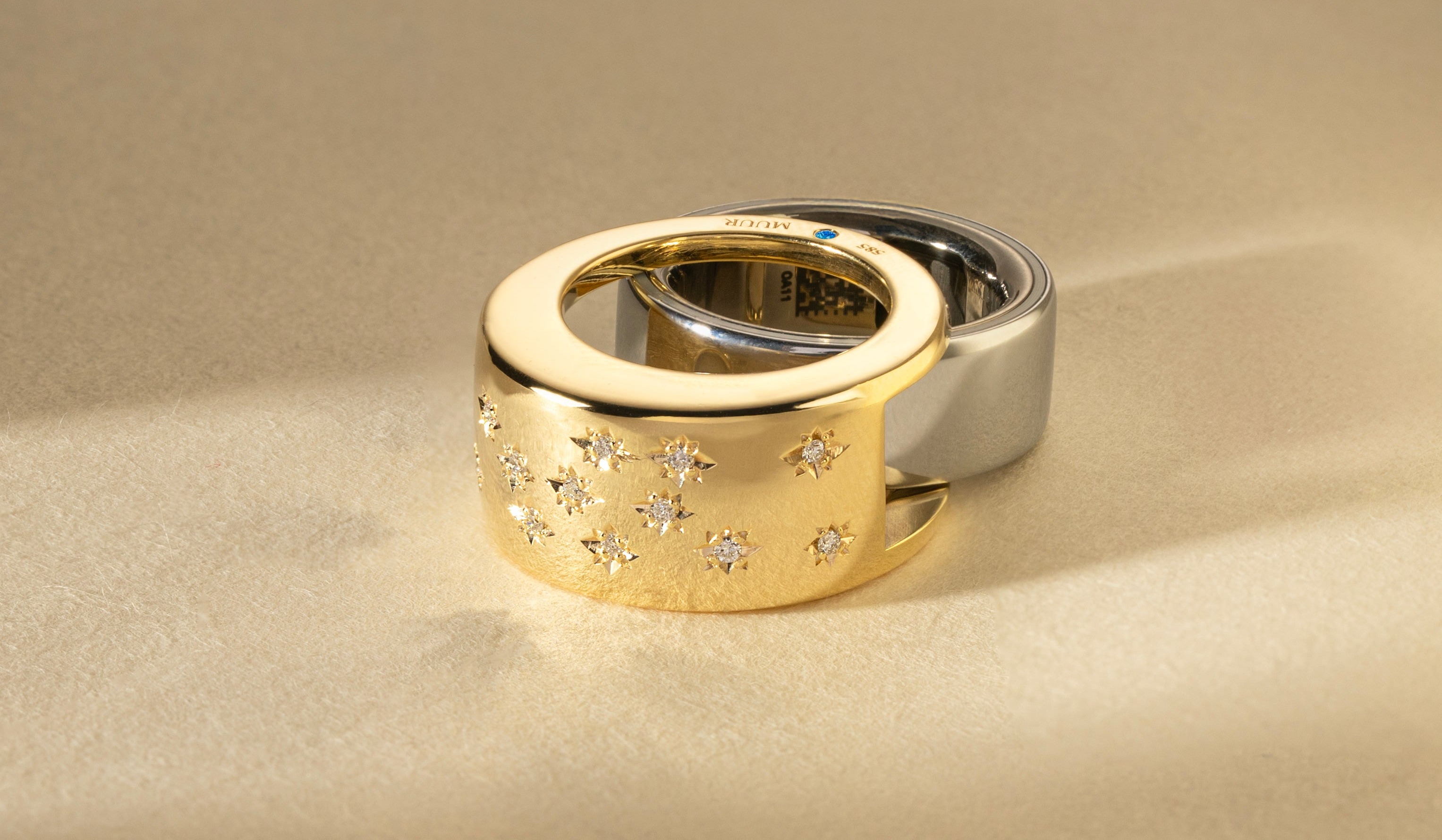 A solid 14k gold enhancer, its inner hallmark and star-set diamonds visible, nested with the bare titanium smart ring it covers, real gold doing the jewelry work while the electronics hide inside.